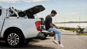 Owner of a used Nissan pickup truck sits on the tailgate while using his phone.