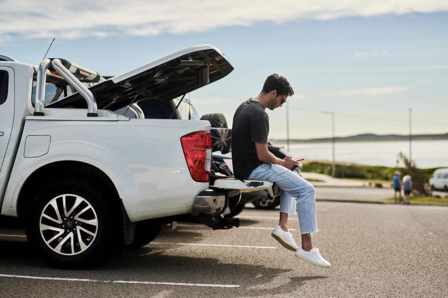 Owner of a used Nissan pickup truck sits on the tailgate while using his phone.
