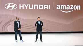 Two Amazon and Hyundai execs talk on stage at the 2023 LA Auto Show with Hyundai and Amazon logos behind them