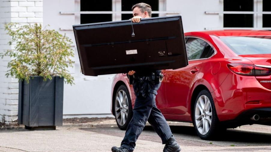 A police officer confiscating a TV set in a fraud case, reminiscent of civil asset forfeiture