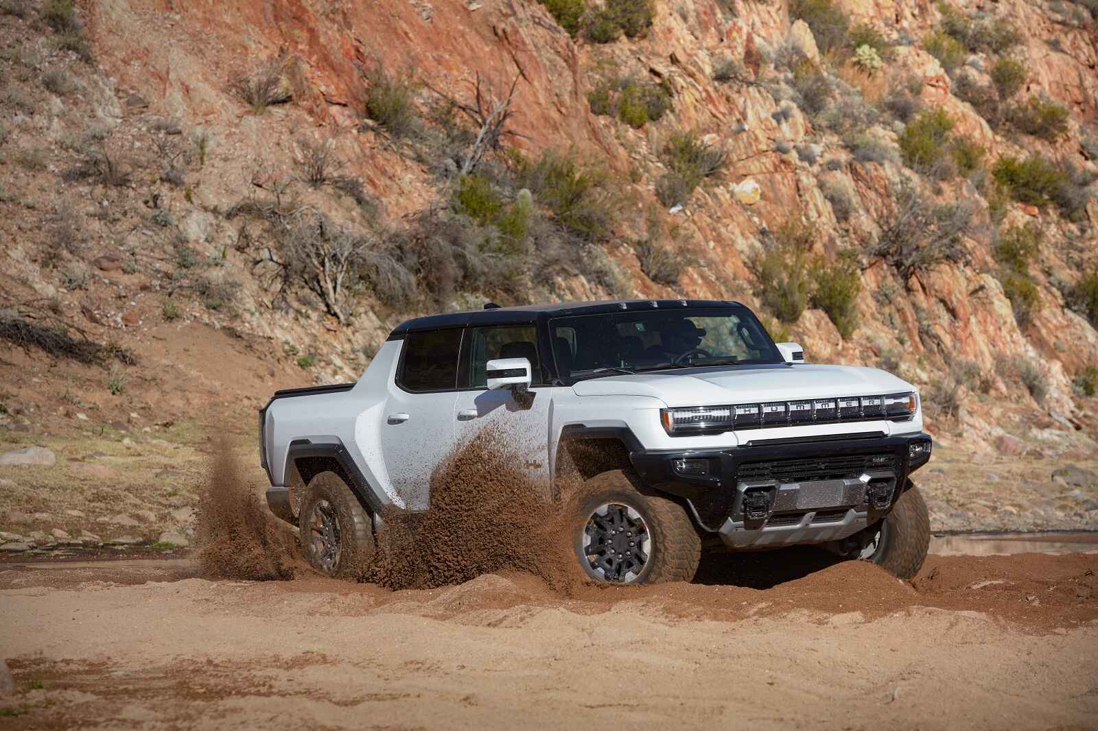 A white GMC Hummer EV Pickup kicks up dirt in a dusty terrain