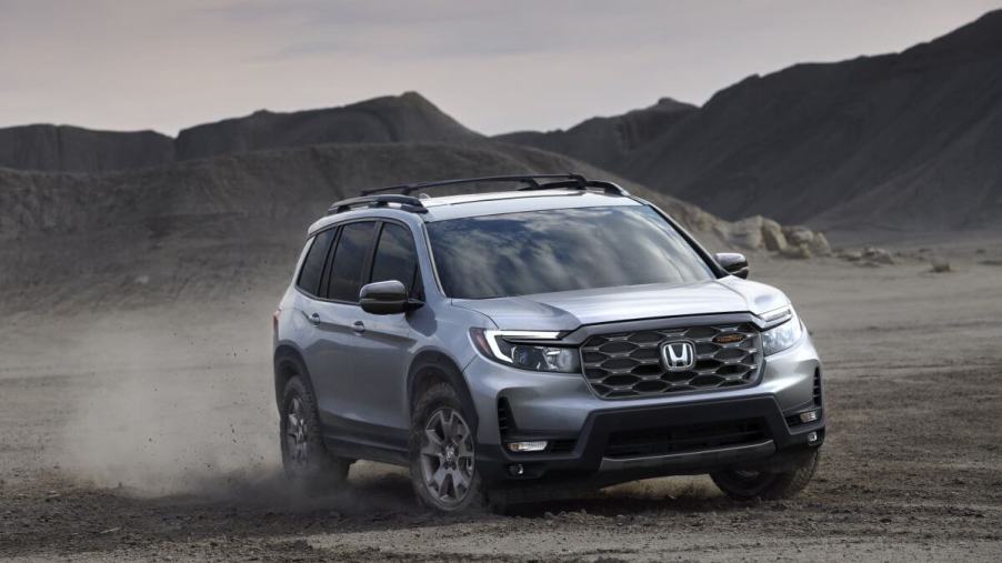 A 2024 Honda Passport TrailSport off-road midsize SUV model kicking up dust as it drives on dirt
