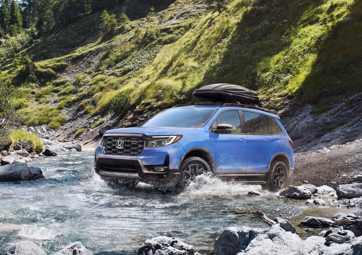 A 2024 Honda Passport TrailSport midsize off-road SUV model traversing a river in grassy mountains