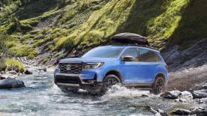 A 2024 Honda Passport TrailSport midsize off-road SUV model traversing a river in grassy mountains