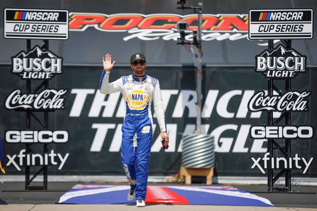 Chase Elliott walks onto the NASCAR track through banner framework touting sponsor logos