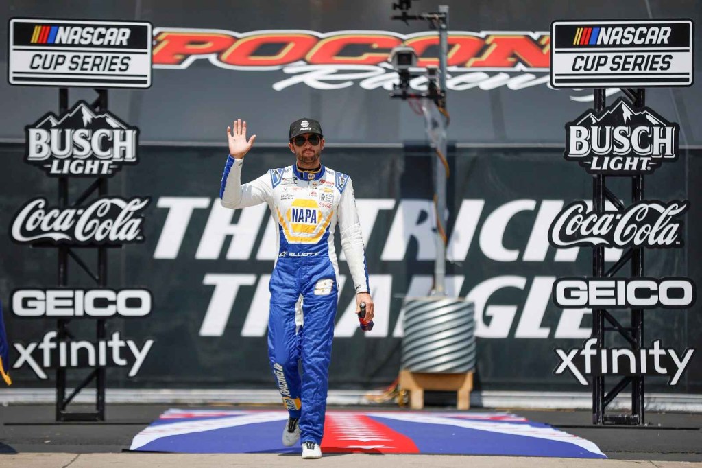 Chase Elliott walks onto the NASCAR track through banner framework touting sponsor logos