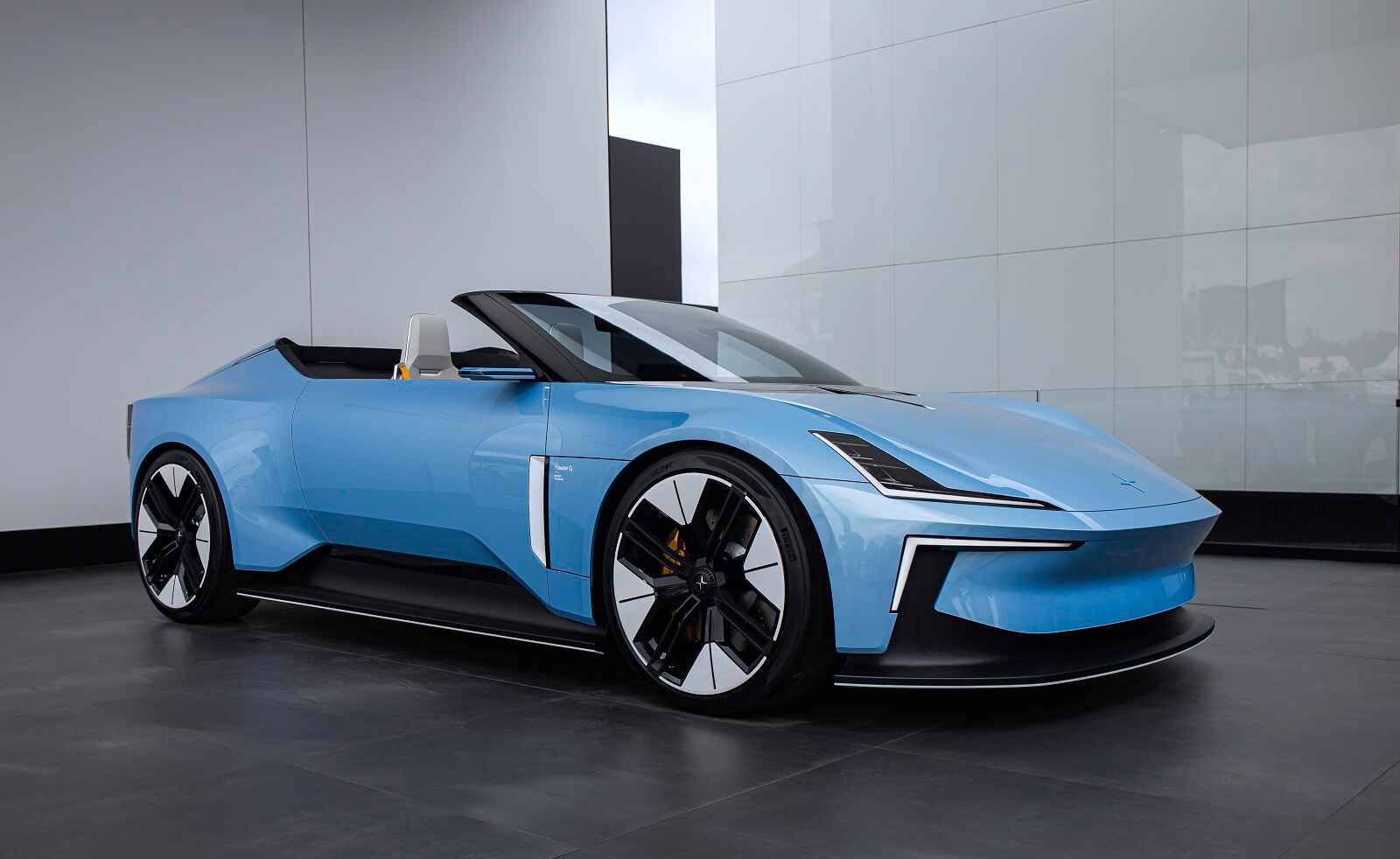 A blue convertible Polestar O2 is shown parked in right front profile view on a showroom floor