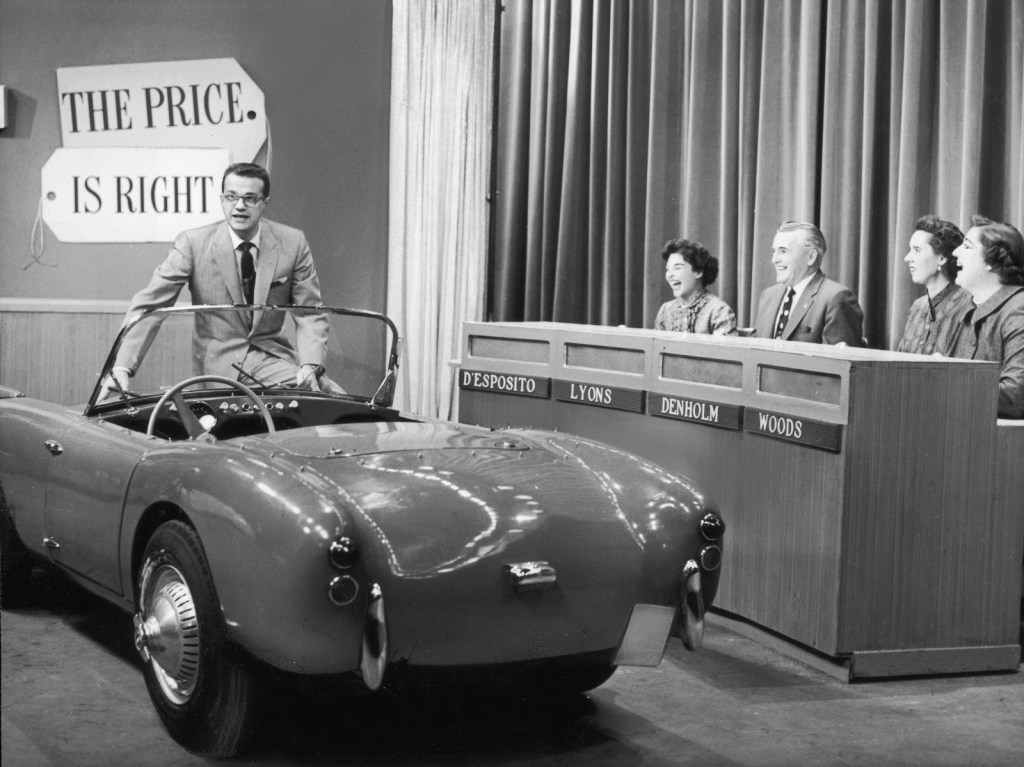 A greyscale image of a new roadster being driven onto the set of The Price is Right gameshow in 1960
