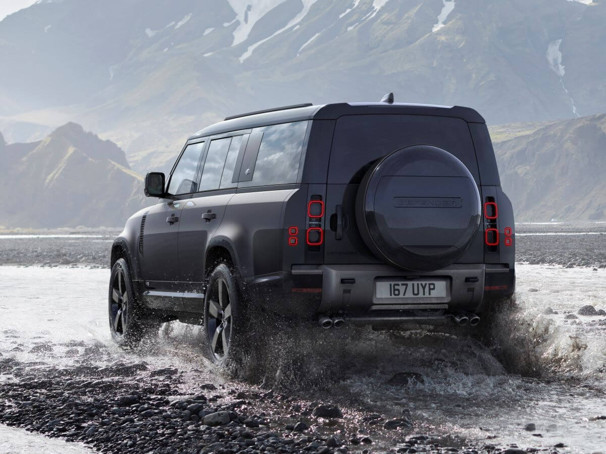 An exterior rear shot of a 2024 Land Rover Defender 130 V8 midsize off-road SUV model driving through water