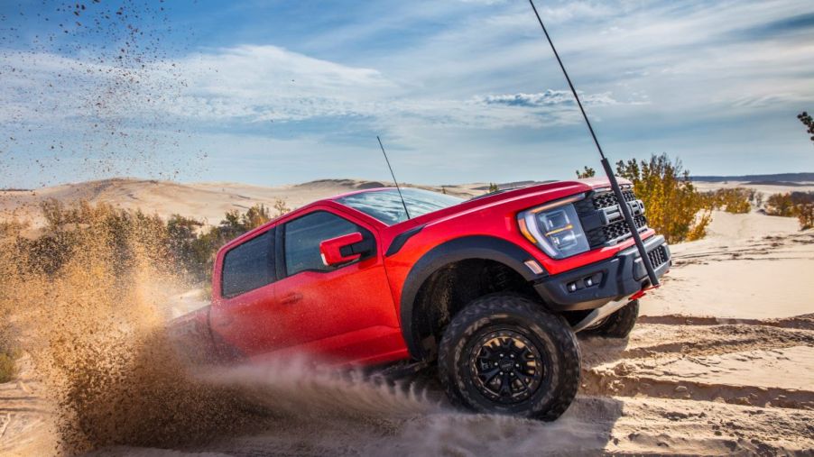 A 2023 Ford F-150 Raptor R full-size pickup truck model driving in sand off-road with a red flag attached