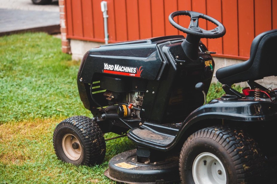 Ride-on tractor-style lawn mower parked against a red building.