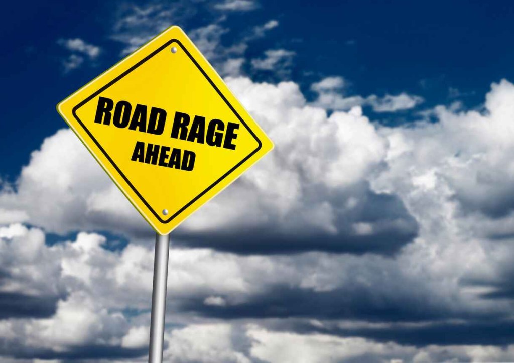 A yellow signed with "road rage ahead" in large lettering with blue sky and puffy clouds in the background