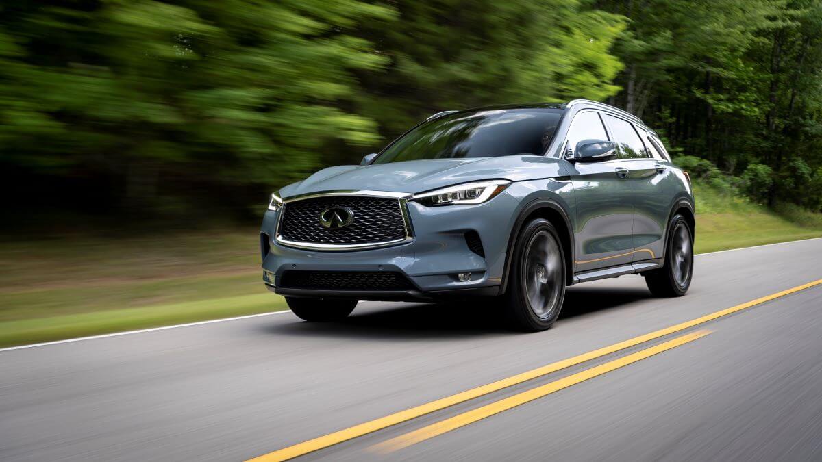 A 2024 Infiniti QX50 compact luxury SUV model driving on a forest highway