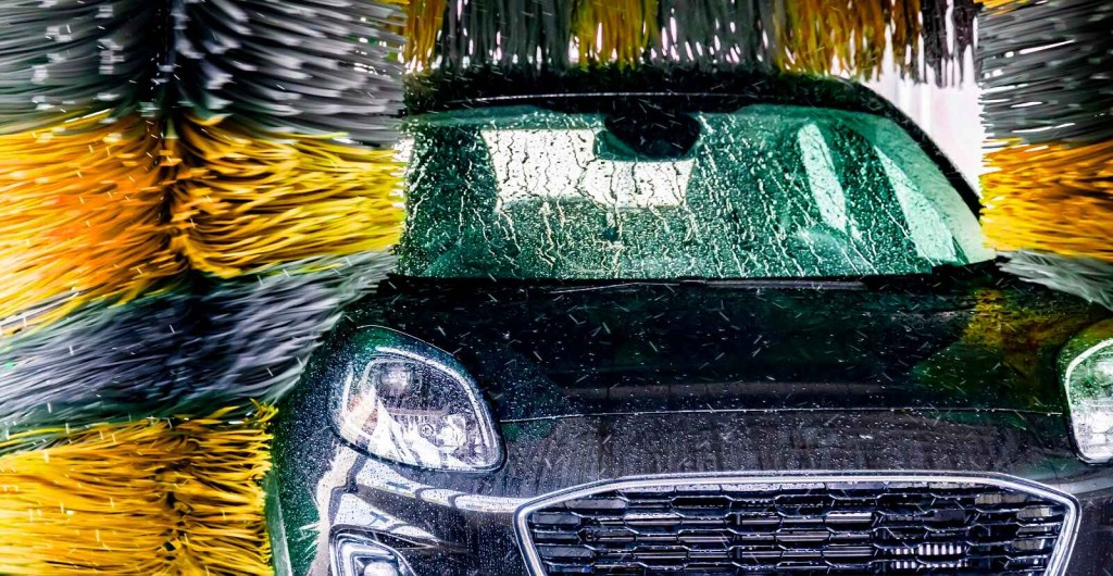 A black car shown making its way through a touch car wash with blue and yellow striped brushes