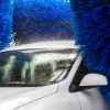 A white car shown in close left front angle in a touch car wash with blue brushes