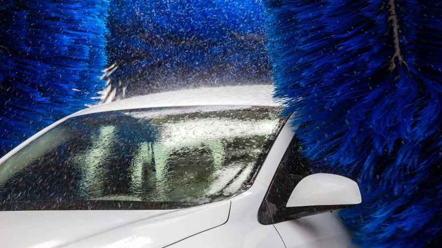 A white car shown in close left front angle in a touch car wash with blue brushes