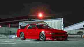 A red Toyota Mk3 Supra is shown in a parking lot at night.