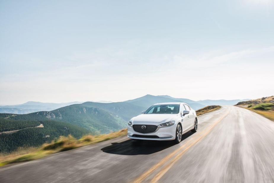 A 2020 Mazda6 midsize sedan model driving down a country highway near forest mountains