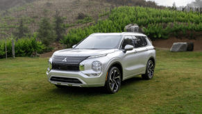 A 2024 Mitsubishi Outlander compact SUV model parked in a grass field surrounded by trees