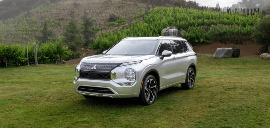 A 2024 Mitsubishi Outlander compact SUV model parked in a grass field surrounded by trees