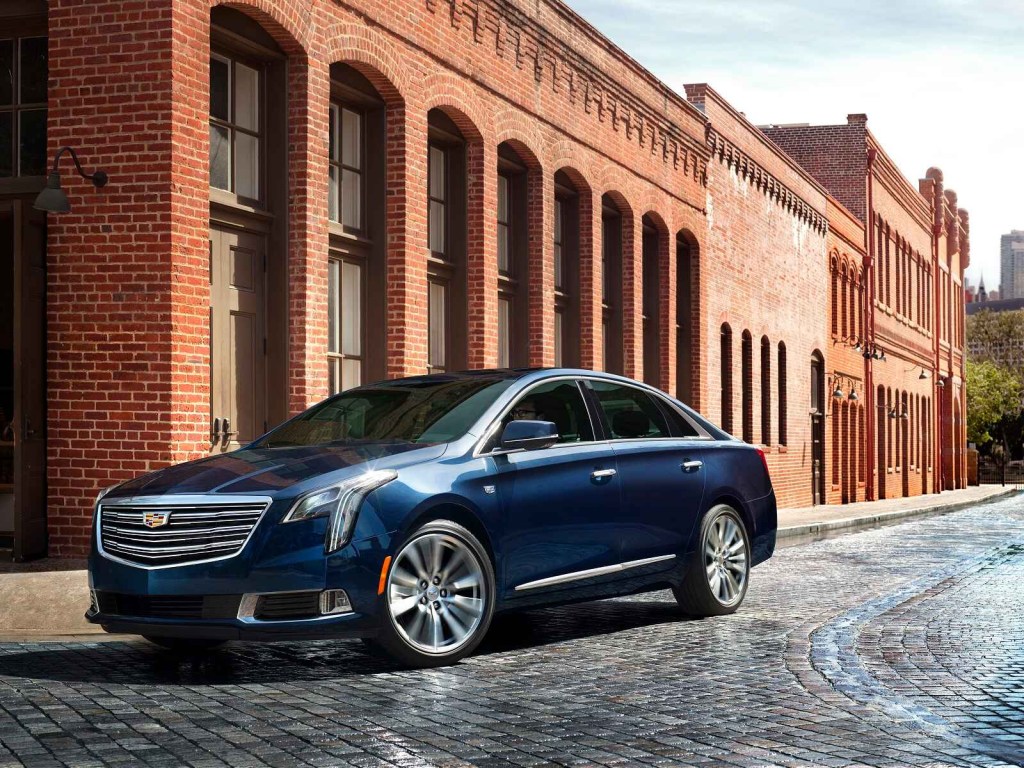 A blue 2019 Cadillac XTS luxury sedan is shown parked at a left front angle in front of a brick building
