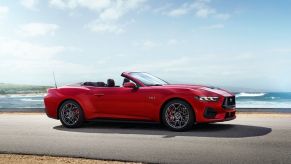 A bright-red 2024 Ford Mustang GT Convertible shows off its soft top by the coast.