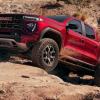 Red 2024 GMC Canyon AT4X AEV Edition midsizee pickup truck climbing on rocks while off-roading.
