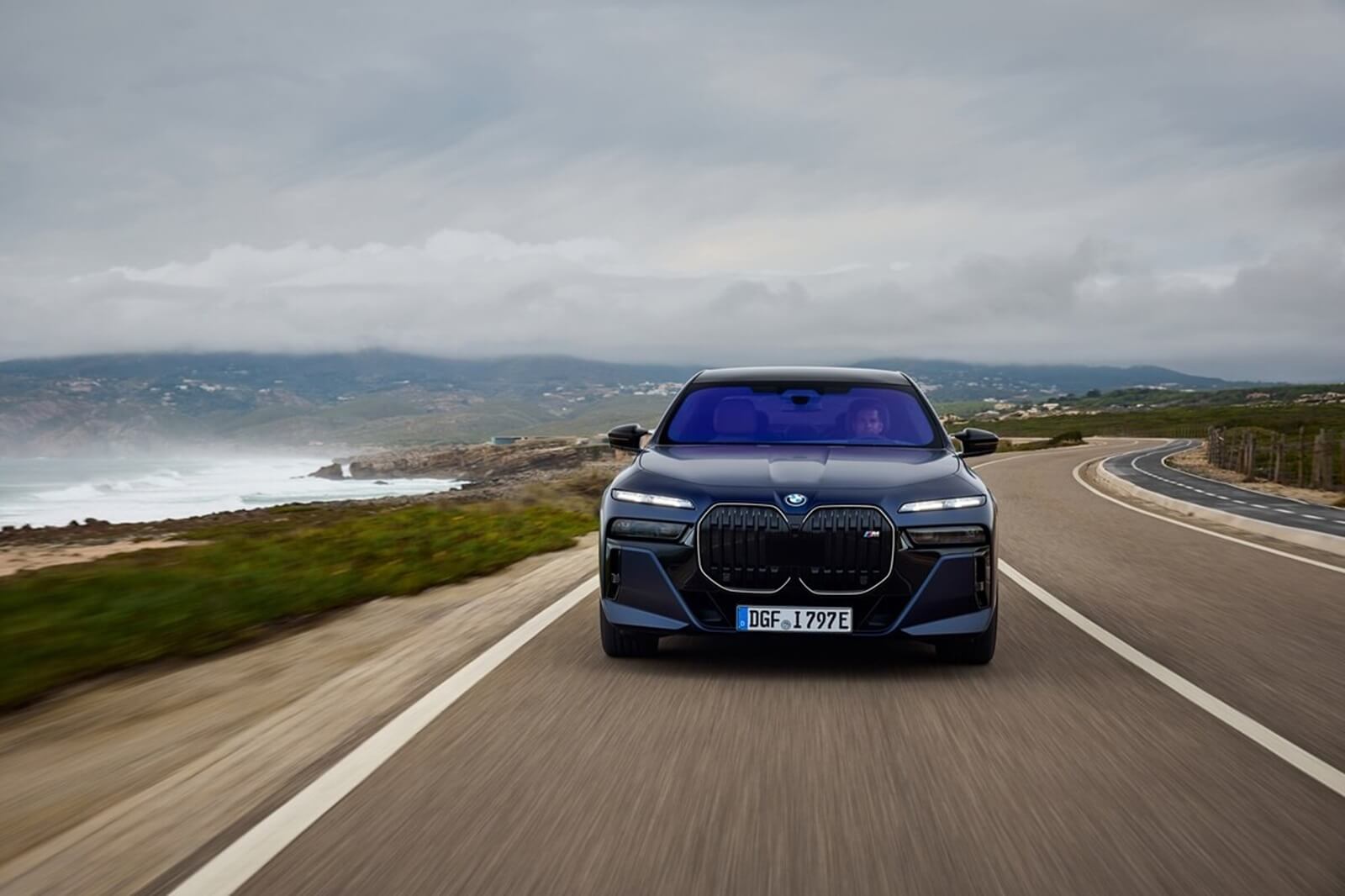 A BMW i7, from the 7 Series that Auto Express considers one of the ugliest cars ever, drives down a coastal road.