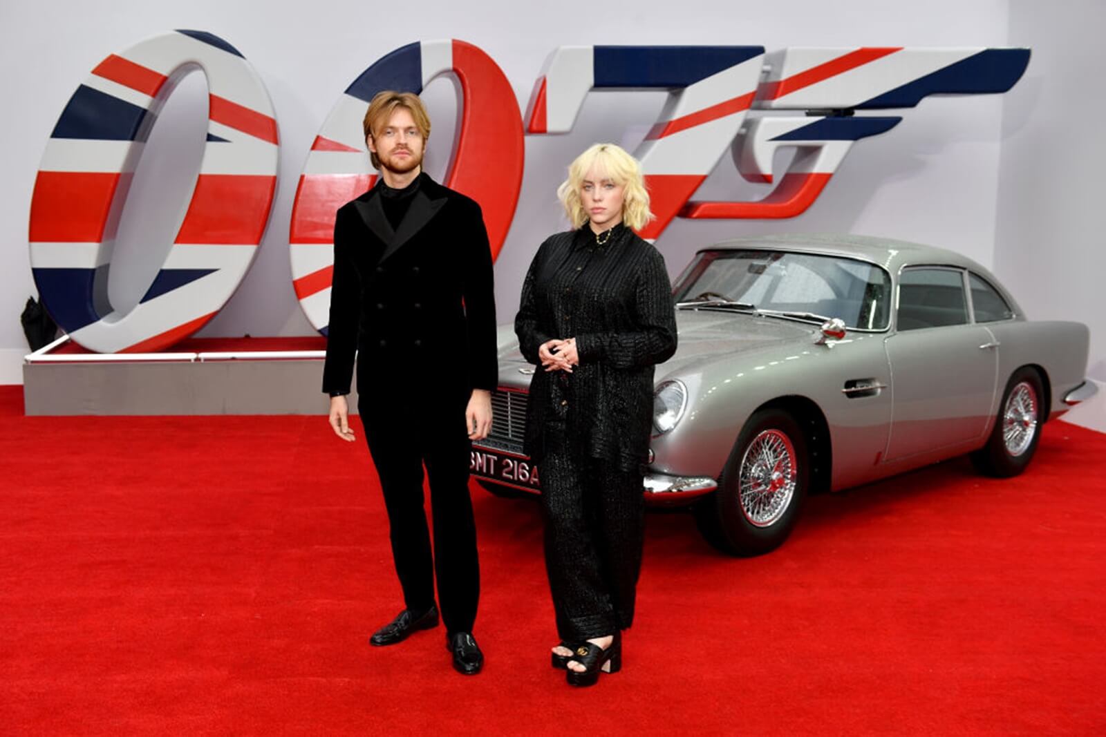 Billie Eilish and Finneas O'Connell pose next to an Aston Martin DB5.