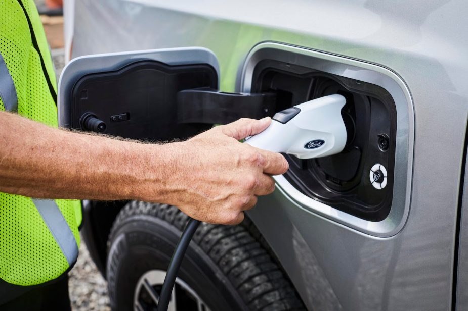 A blue collar worker's hand as they plug an F-150 Lightning electric pickup truck into a Ford Pro charger.