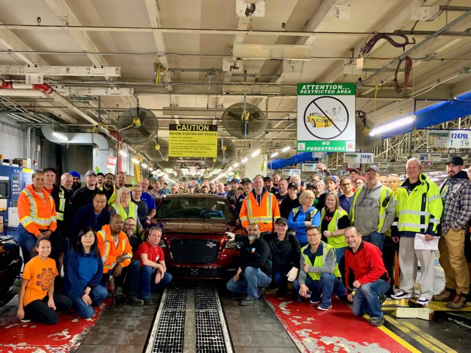 A row of factory workers pose with the final Hemi V8 powered Chrysler 300C sedan.