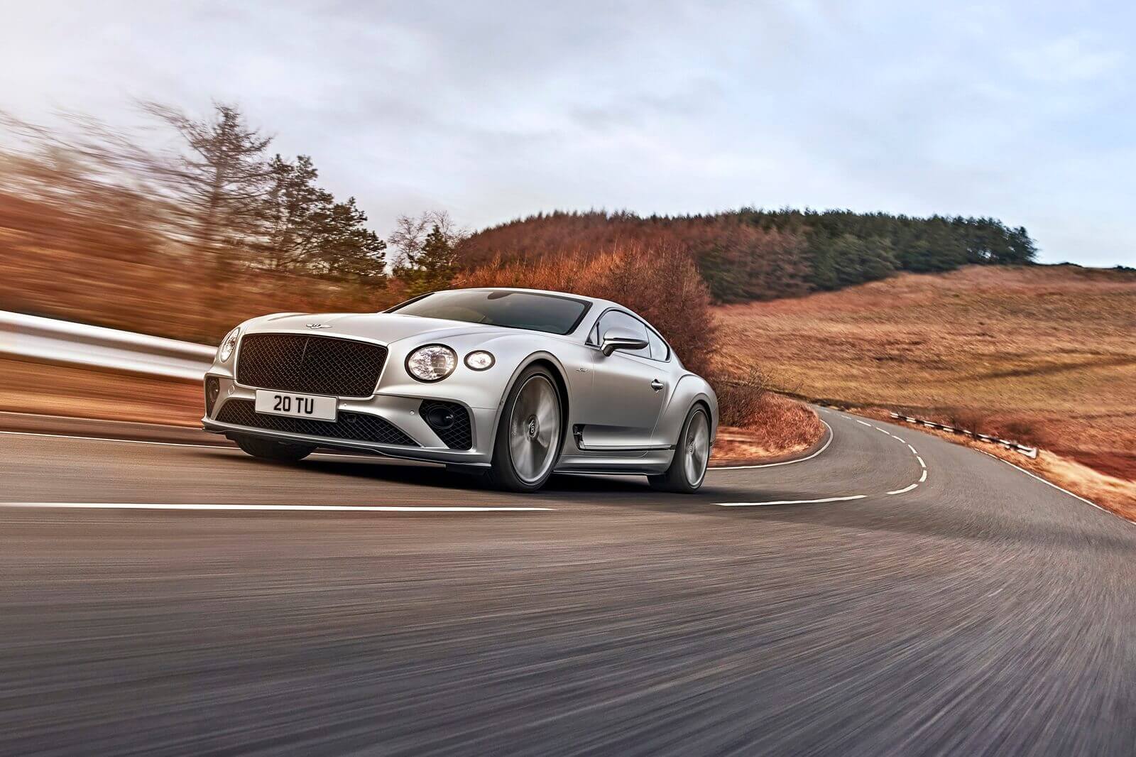 A silver Bentley Continental GT Speed cruises down an open road.