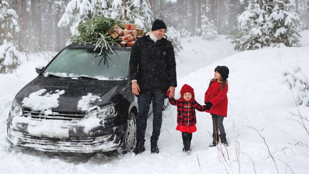 Father and his daughters are carrying a Christmas tree from the forest. Christmas tree and gifts on the roof of the car.