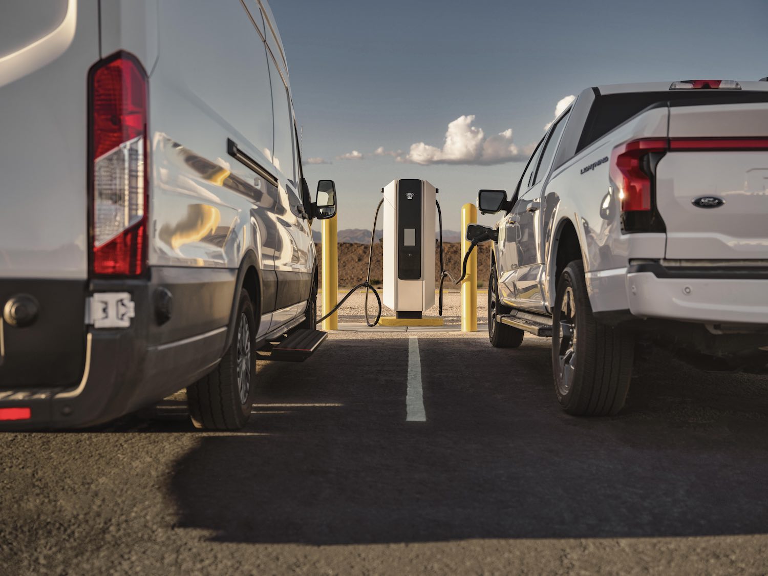 The rear bumpers of an electric F-150 and Ford Transit van both plugged into a charger.