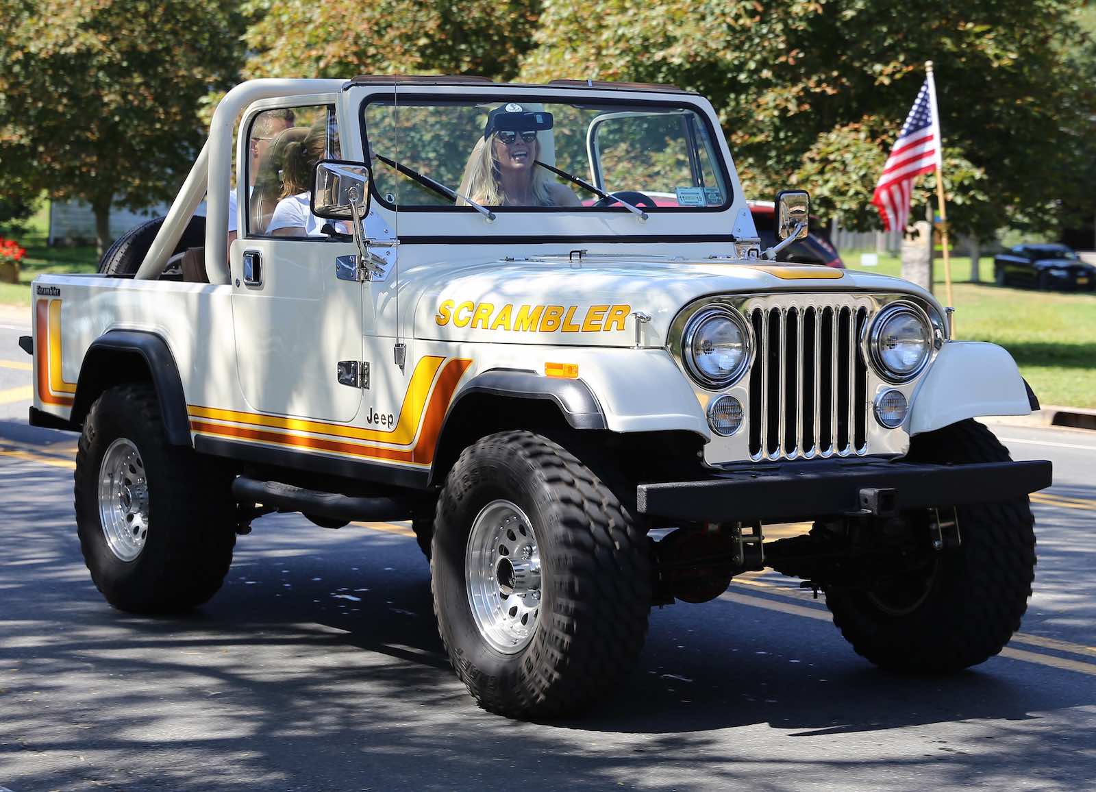 Two women drive a white Jeep down the road.