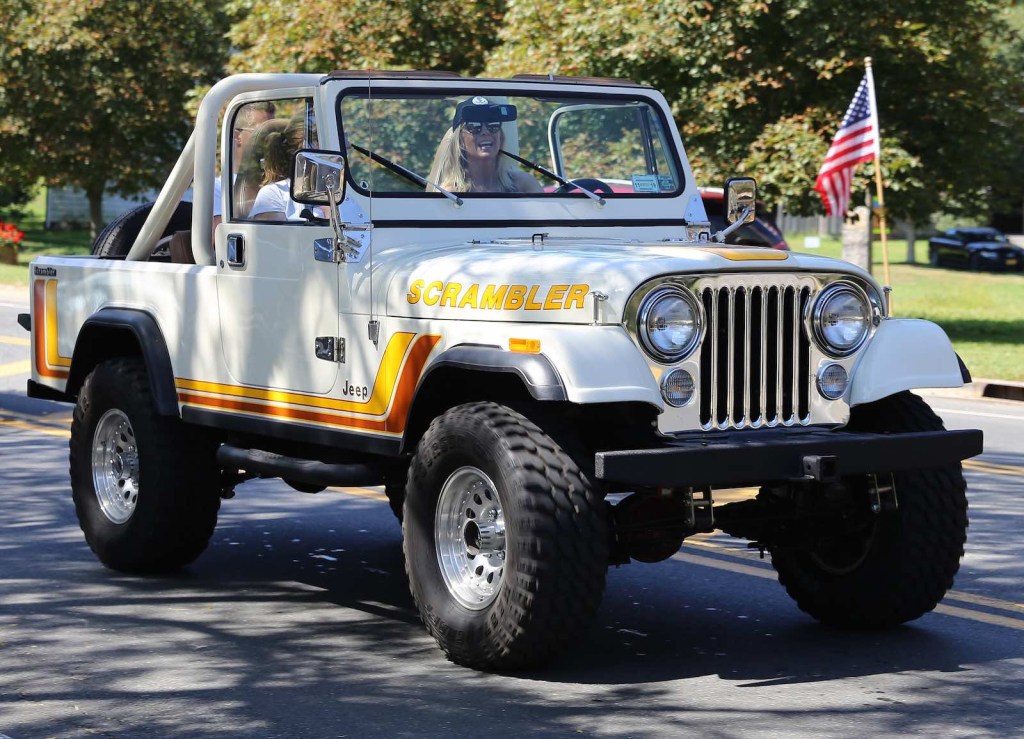 Two women drive a white Jeep down the road.