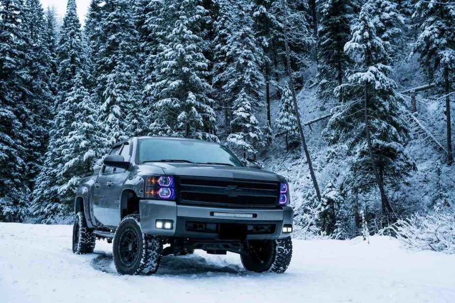 Lifted custom Chevrolet truck parked in the snow in front of trees.