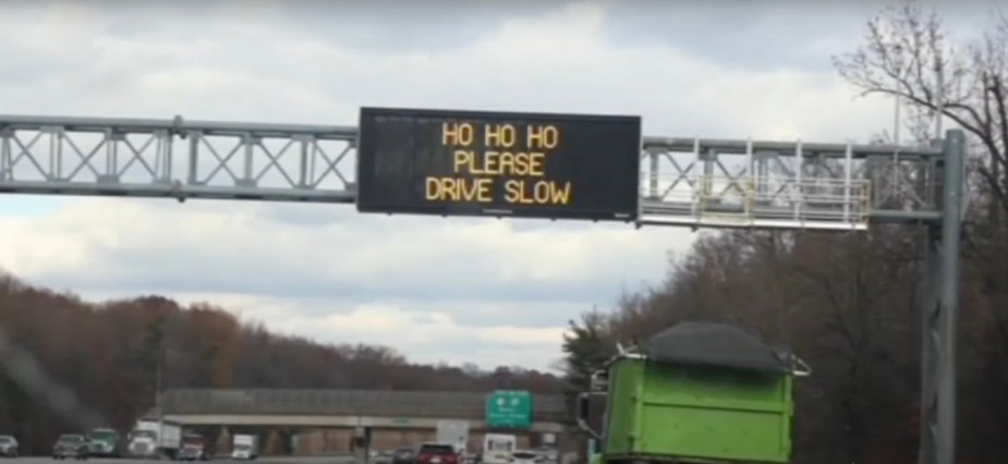 A Road sign above the New Jersey highway that reads "Ho Ho Ho Please Drive Slow"