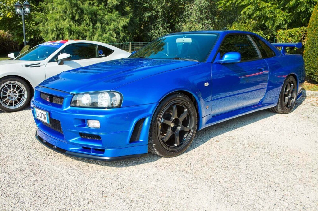 A blue Nissan Skyline GT-R R34 import car sits in a lot.