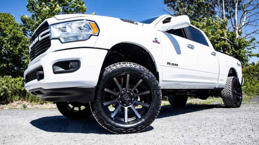 The aftermarket rims under a lifted white Ram pickup truck parked in a lot.