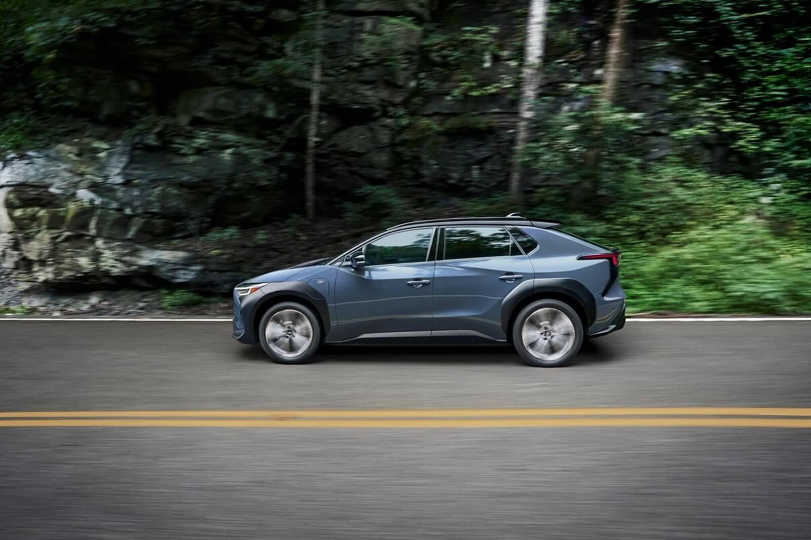 A 2023 Subaru Solterra drives through a wooded area.