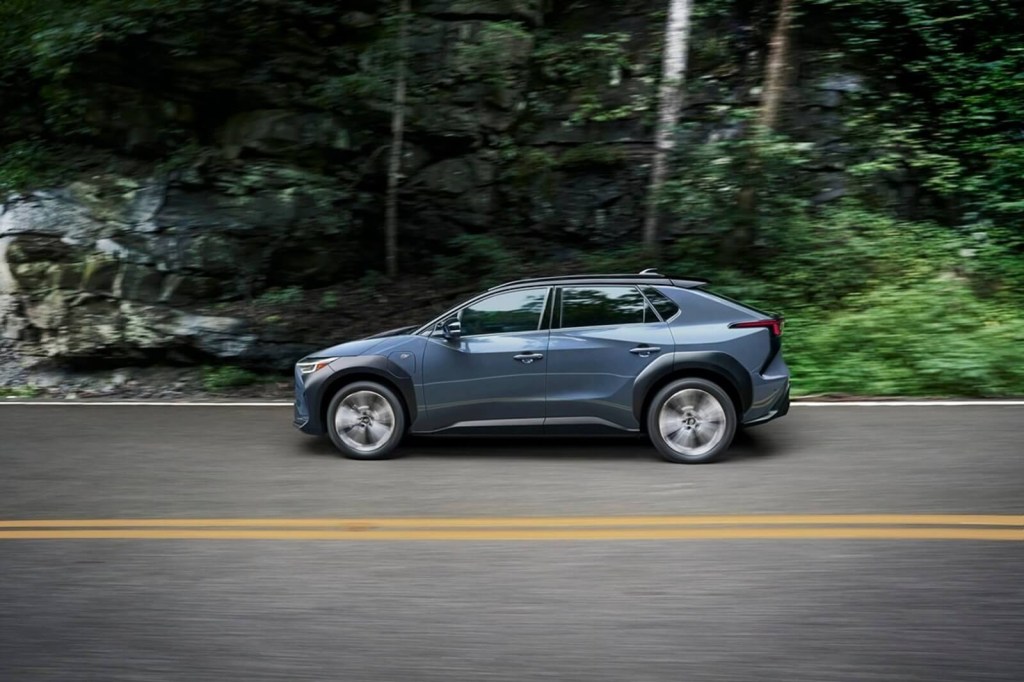 A 2023 Subaru Solterra drives through a wooded area.