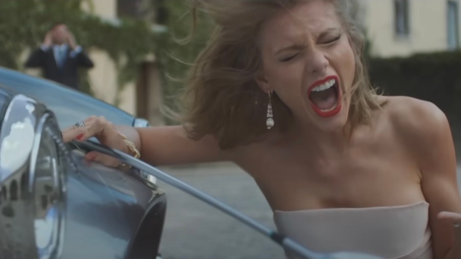 Taylor Swift sings next to a smashed Shelby Cobra sports car.