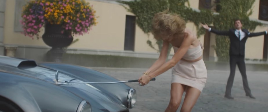 Taylor Swift swinging a golf club down onto the hood of a Shelby Cobra sports car during her music video.