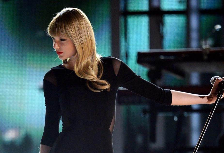 Taylor Swift sings on stage in a black shirt.