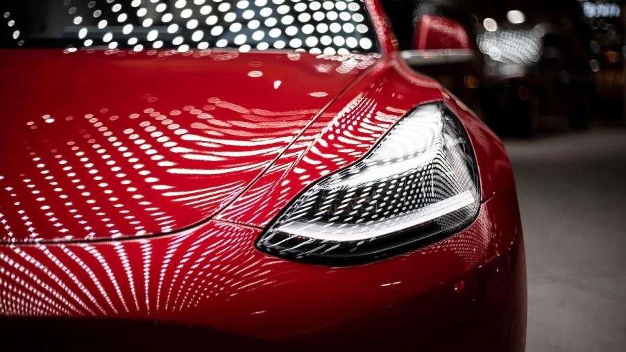Hood and headlight of a red Tesla Model 3.