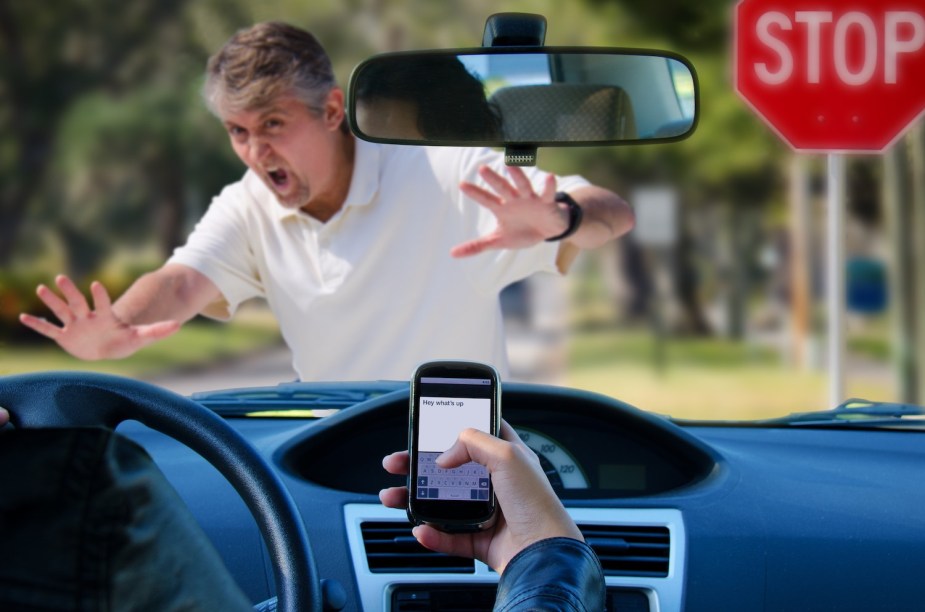 A pedestrian holds up his hands before being hit by a driver who is being unsafe by texting.