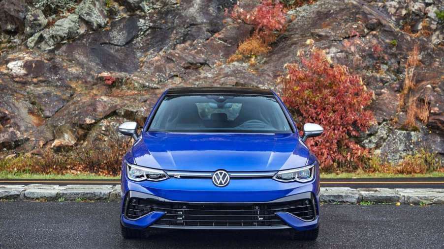 A blue Volkswagen Golf R sits by a rock wall.