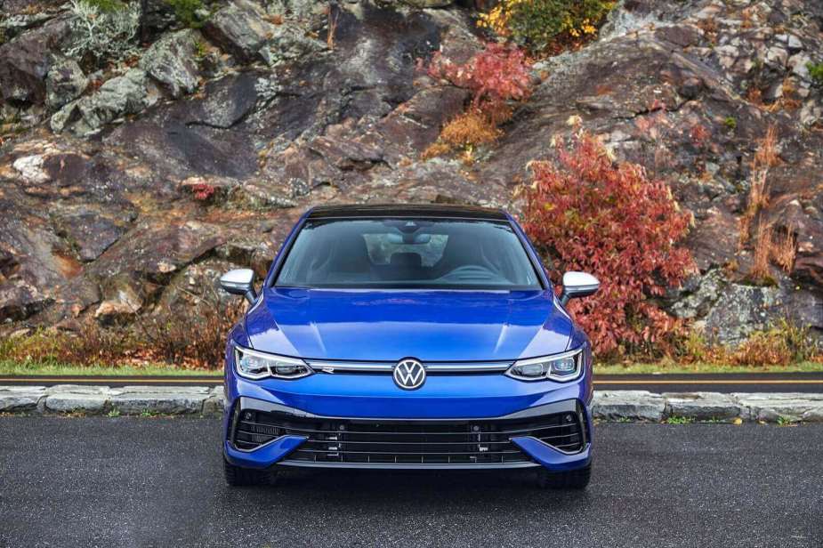 A blue Volkswagen Golf R sits by a rock wall.