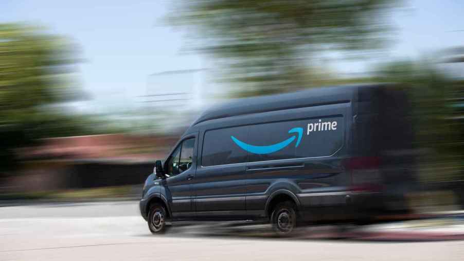 A blue Amazon Prime delivery van is shown in left side view driving fast with a blurred background